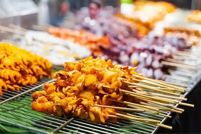 Variety of colorful Thai street food dishes including grilled meats, skewers, and desserts at a bustling Thailand night market.