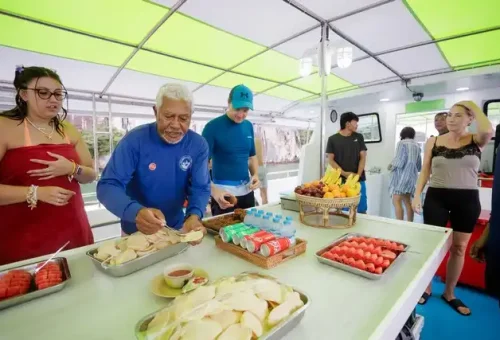 Friendly tour guide offering a tray of fresh fruits and traditional Thai snacks to guests on the boat during the twilight sea canoe tour