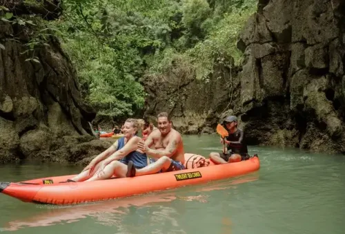 Guests relaxing in canoes as local paddle guides navigate through calm waters and sea caves during the twilight sea canoe tour in Phang Nga Bay