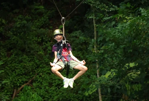 Adventurer gliding across a high zipline with arms outstretched, surrounded by Phuket’s lush jungle at Flying Hanuman