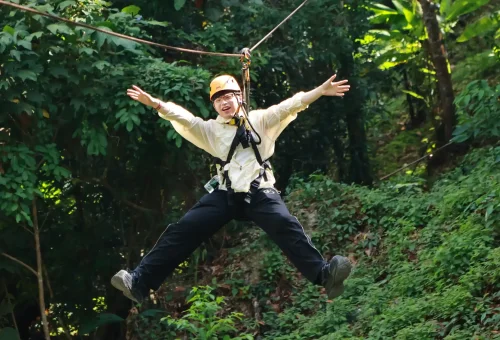 Adventurer soaring high above the jungle on a zipline at Flying Hanuman, enjoying the breathtaking view and adrenaline rush