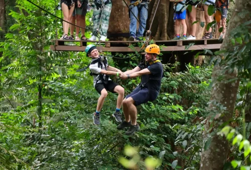 Adventurer ziplining through the lush Phuket jungle at Flying Hanuman with arms spread wide, mimicking an eagle in flight