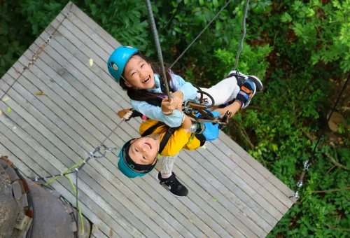 Young child enjoying a safe and exciting zipline ride at Flying Hanuman in Phuket, guided by a trained staff member