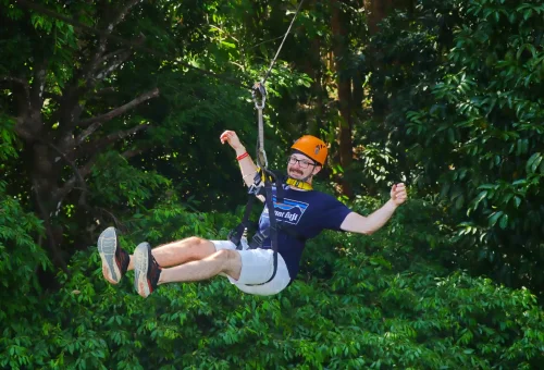 Smiling family and couple ziplining side by side through the lush jungle canopy at Flying Hanuman in Phuket