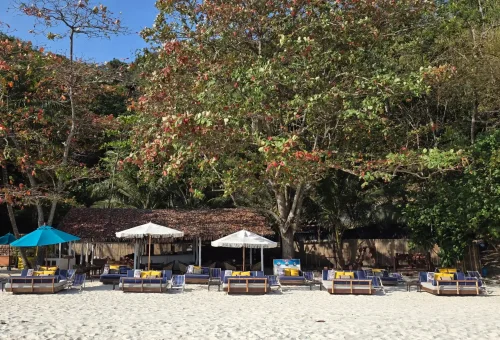 Scenic view of Banana Beach with rows of beach loungers under umbrellas, soft white sand, and clear turquoise waters in the background
