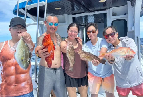 Proud customer holding up a freshly caught fish on a fishing boat during a game fishing and trolling excursion in Phuket