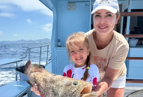 Cheerful customer proudly holding a freshly caught fish on a game fishing boat during a trolling trip in the waters of Phuket