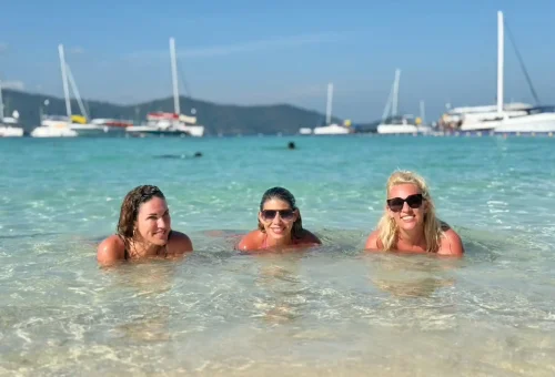 Three ladies enjoying the turquoise sea at Kahung Beach, Coral Island, with clear skies and tropical waters in the background