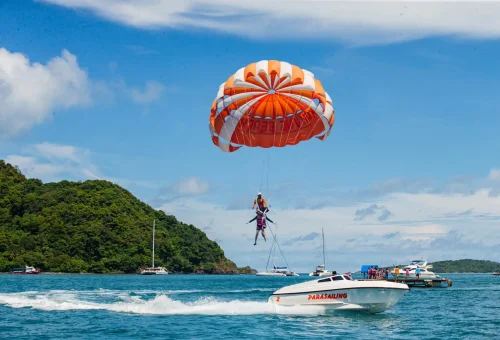 Tourist parasailing high above the turquoise waters at Kahung Beach, Coral Island, with a parachute against a clear blue sky