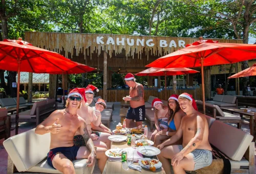 Tropical Christmas scene at Kahung Beach with festive decorations, palm trees, and beachgoers celebrating by the sea