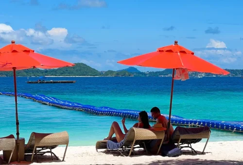 Visitors lounging on beach chairs under umbrellas at Kahung Beach, Coral Island, with waves gently rolling in