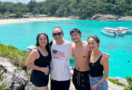 Happy customer relaxing on the beach of Raya Island with clear blue sea and white sand in the background.