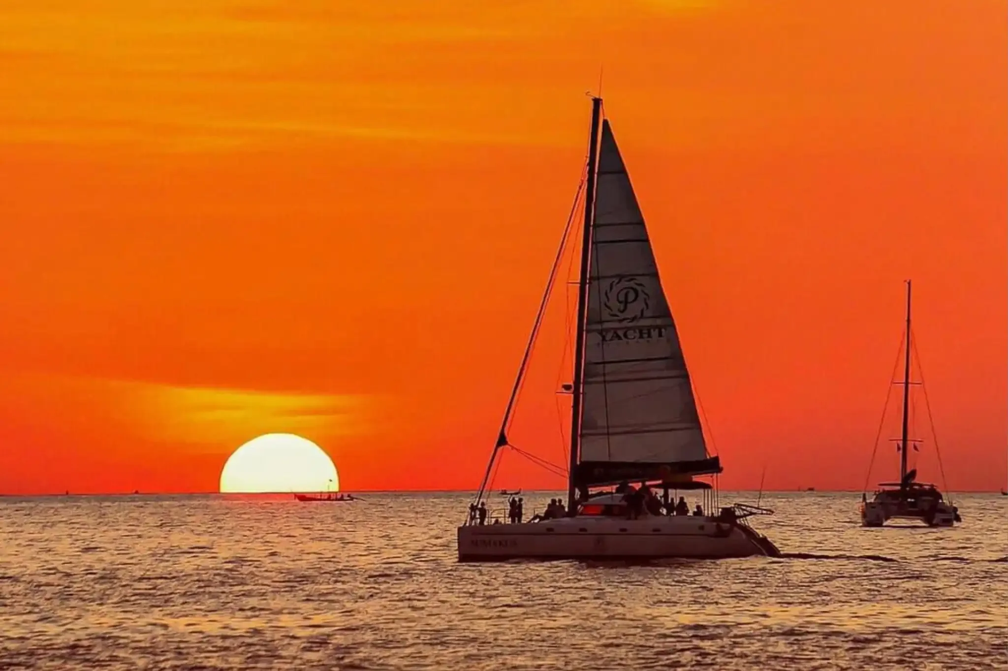 Luxury sailing yacht gliding into the golden sunset near Coral Island and Promthep Cape.