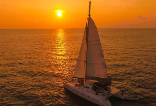 Elegant sailing yacht bathed in sunset light near Promthep Cape and Coral Island.