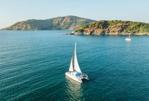 Aerial view of a luxury sailing yacht cruising during sunset near Coral Island and Promthep Cape.