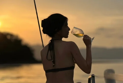 Woman enjoying a glass of wine at sunset on a luxury sailing yacht near Coral Island and Promthep Cape.