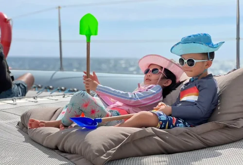 Guests smiling and enjoying the sun on the front deck of a luxury sailing yacht cruising toward Racha and Coral Islands in Phuket.