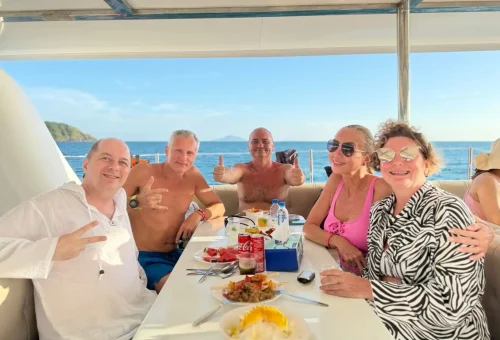 Cheerful group of tourists enjoying music, drinks, and ocean views on a luxury sailing yacht cruising to Racha and Coral Islands, Phuket.