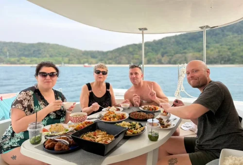 Group of joyful passengers enjoying the sun and ocean breeze on the upper deck of a luxury sailing yacht near Racha and Coral Islands, Phuket.
