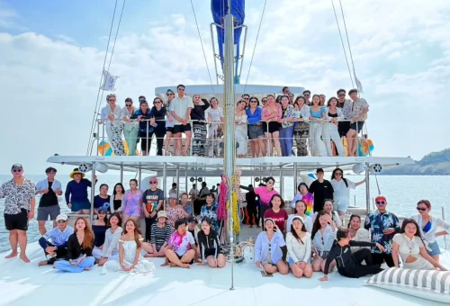 Joyful group of tourists enjoying drinks and sea views on the deck of a luxury sailing yacht heading to Racha and Coral Islands, Phuket.