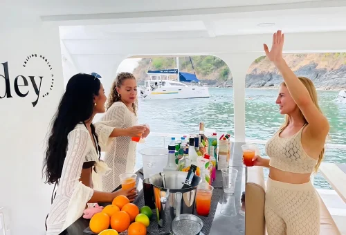 Smiling guests lounging and chatting on the sun deck of a luxury sailing yacht cruising toward Racha and Coral Islands in Phuket.