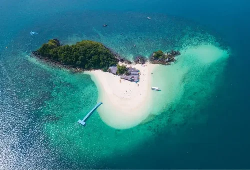 Aerial view of Khai Nok Island with turquoise waters, white sandy beach, and small beachfront buildings, taken during the Phi Phi Island speed catamaran tour by Phuket Travel Store