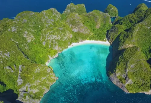 Stunning view of Maya Bay at Phi Phi Leh Island with calm turquoise water, white sandy beach, and dramatic limestone cliffs, captured during the speed catamaran tour by Phuket Travel Store
