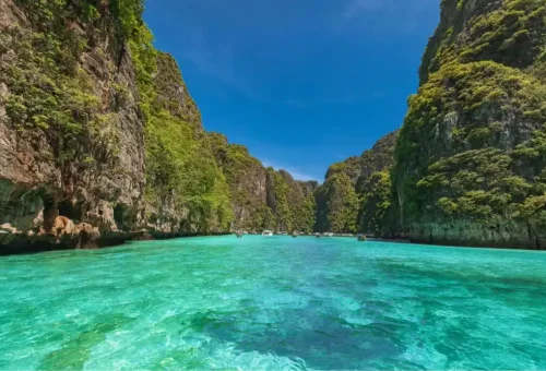 Tour boat floating in the emerald waters of Pileh Lagoon, surrounded by steep limestone cliffs at Phi Phi Leh Island, part of the speed catamaran tour by Phuket Travel Store