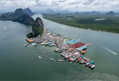 Aerial view of Koh Panyee floating village with houses built on stilts over the sea, surrounded by limestone cliffs in Phang Nga Bay