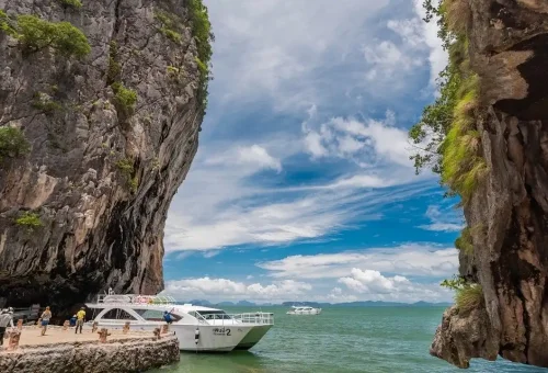 Speed catamaran berthed near the iconic limestone karst of James Bond Island, surrounded by emerald-green water in Phang Nga Bay