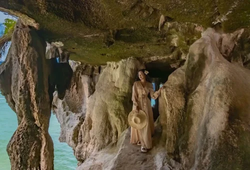 A woman posing inside a limestone cave at James Bond Island, surrounded by dramatic rock formations and soft natural lighting