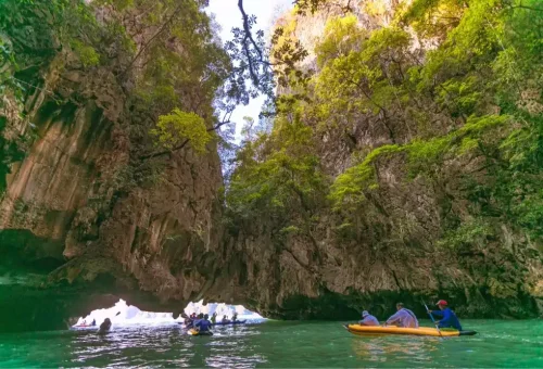 Tour group canoeing through the calm emerald-green waters of Hong Island Lagoon, surrounded by limestone cliffs, during the James Bond Island canoe tour by Phuket Travel Store