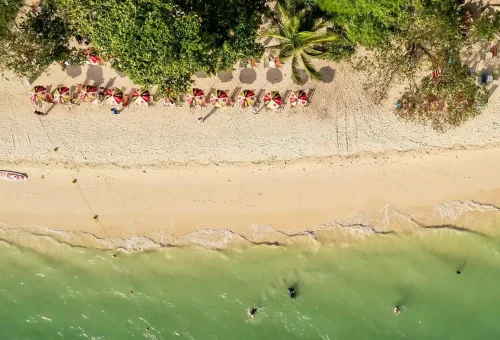 Aerial view of Rang Yai Island beach with soft white sand, clear turquoise shoreline, and tropical palm trees, part of the James Bond Island tour by Phuket Travel Store