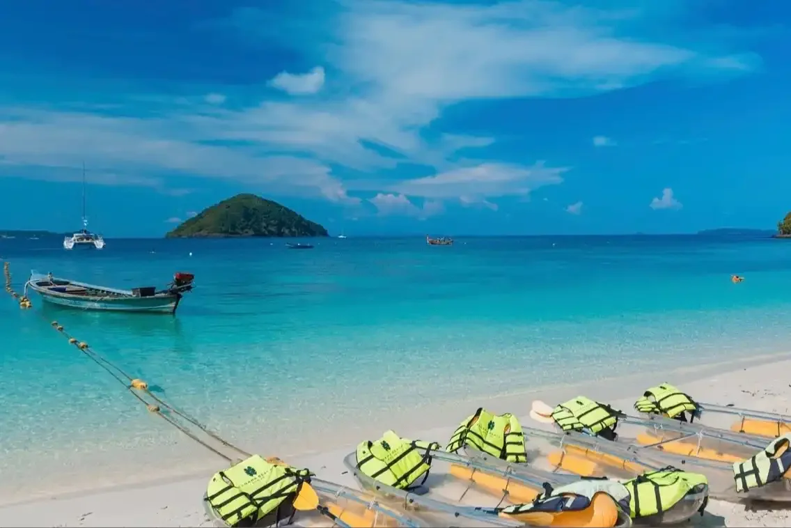 Glass-bottom kayaks resting on the sandy beach of Coral Island, with clear turquoise waters in the background