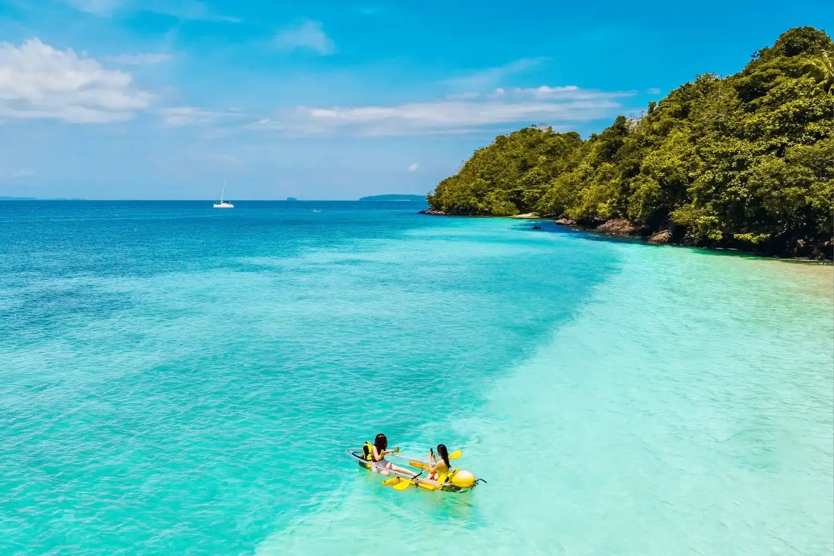 Person kayaking in front of the sandy beach at Coral Island, with lush greenery and clear turquoise sea