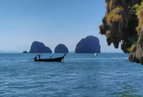 Traditional longtail boat cruising through Phang Nga Bay near James Bond Island with limestone cliffs in the background