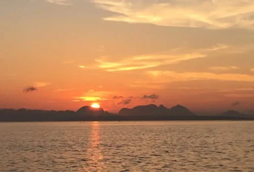 Golden sunrise lighting up the limestone cliffs of Phang Nga Bay with longtail boats in the distance