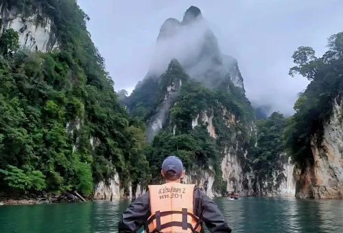 Traveler admiring the stunning limestone cliffs and emerald waters of Cheow Lan Lake in Khao Sok National Park