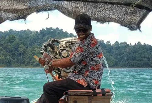 Friendly longtail boat captain smiling while navigating Cheow Lan Lake in Khao Sok National Park