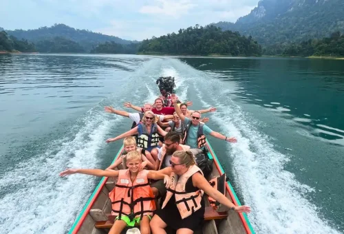 Smiling tourist on a longtail boat cruising Cheow Lan Lake surrounded by limestone cliffs in Khao Sok National Park