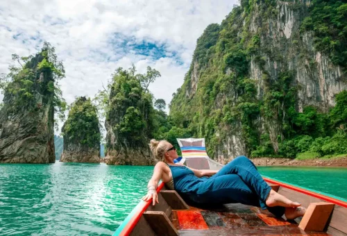 Happy traveler admiring limestone cliffs and emerald waters from a boat on Cheow Lan Lake in Khao Sok National Park