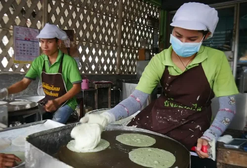Visitor enjoying grilled river prawns while exploring Wat Phra Si Sanphet and taking photos of ancient Buddha heads