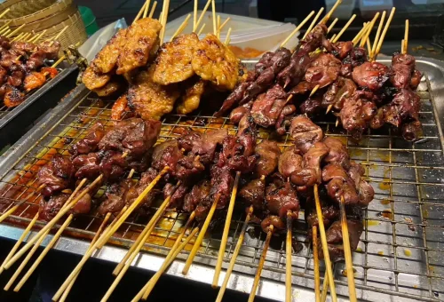 Guest enjoying satay skewers at Pak Khlong Talad flower market during Bangkok Midnight Food Tour by Tuk Tuk with Phuket Travel Store