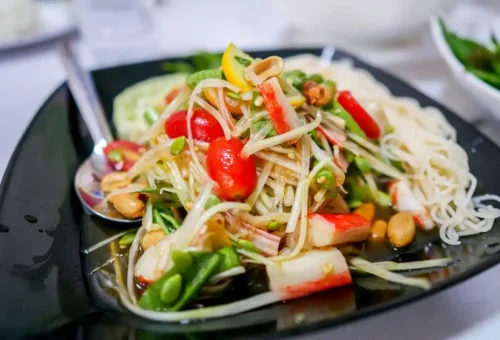 Colorful vegetarian papaya salad with crab sticks, peanuts, and noodles