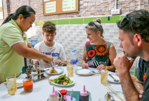 Tour guide serving vegetarian noodles to happy tourists in a Bangkok restaurant