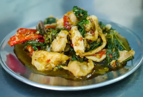 Thai chicken stir-fried with chili, basil, and herbs on a metal plate