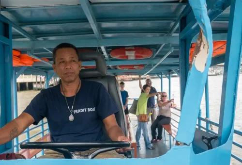 Thai boat driver steering a river ferry with tourists on board