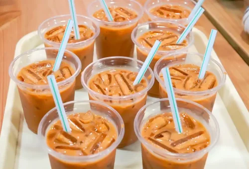 Multiple cups of Thai iced tea with ice and straws on a tray
