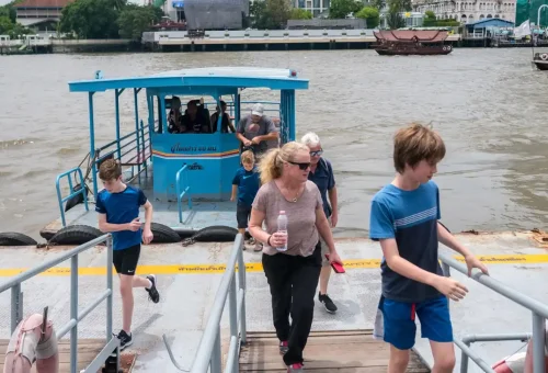 Tourists walking off a blue riverboat onto a pier in Bangkok