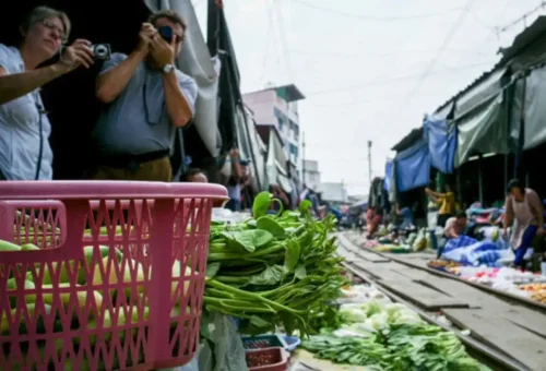 Western tourists photographing vegetables at the Maeklong Railway Market